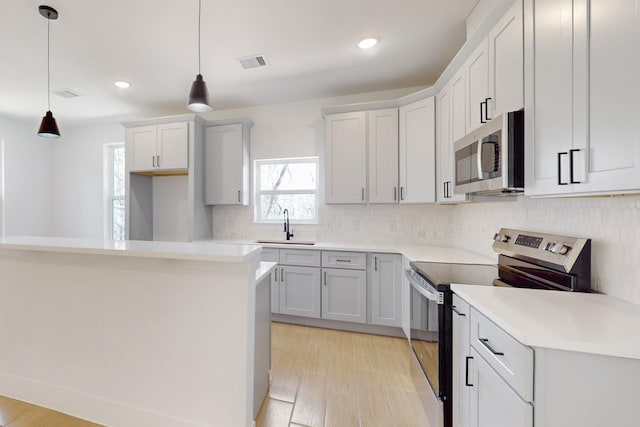 kitchen featuring light wood finished floors, visible vents, hanging light fixtures, stainless steel appliances, and a sink