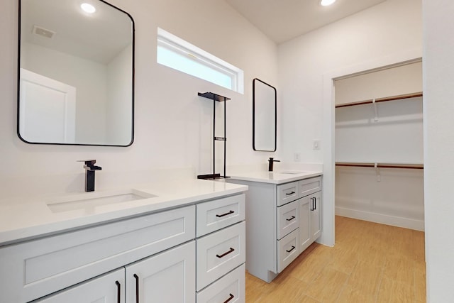 bathroom featuring a spacious closet, two vanities, wood finished floors, and a sink