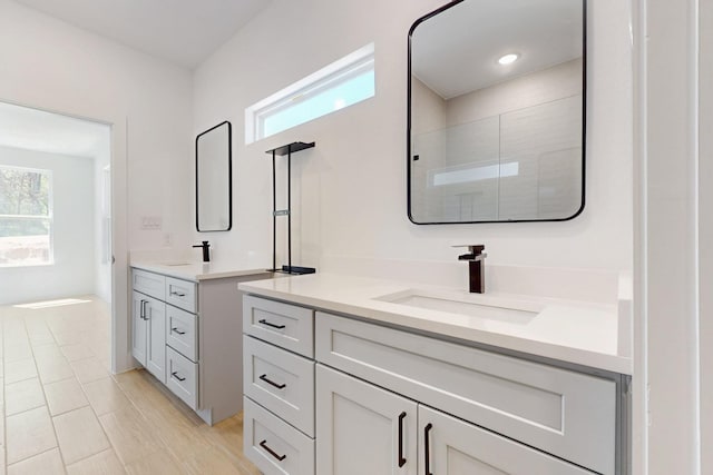 full bathroom featuring a healthy amount of sunlight, a stall shower, two vanities, and a sink