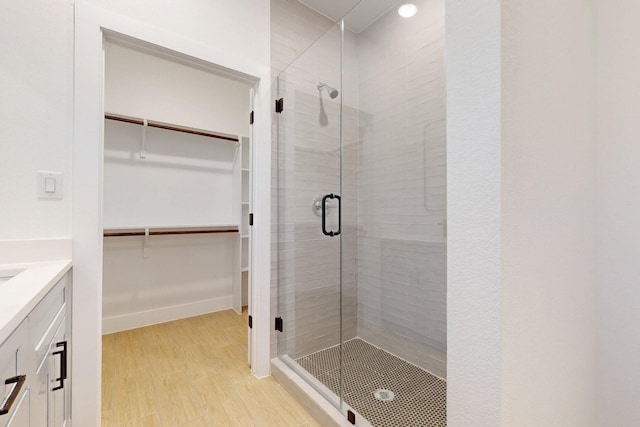 bathroom with a stall shower, vanity, a walk in closet, and wood finished floors