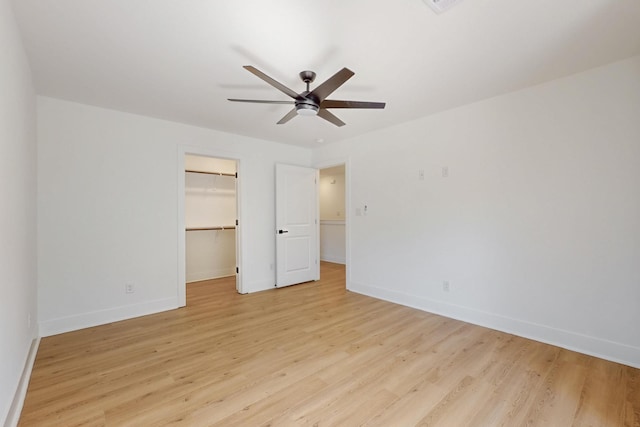 unfurnished bedroom featuring a spacious closet, a closet, baseboards, and light wood finished floors