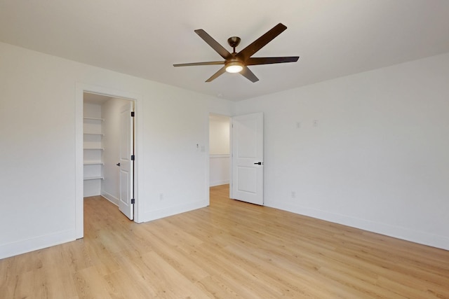 unfurnished bedroom with baseboards, a ceiling fan, light wood-style flooring, and a spacious closet