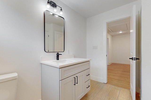 half bathroom with toilet, vanity, baseboards, and wood finished floors