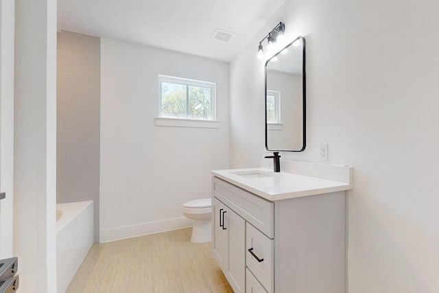 bathroom with visible vents, toilet, a tub, baseboards, and vanity