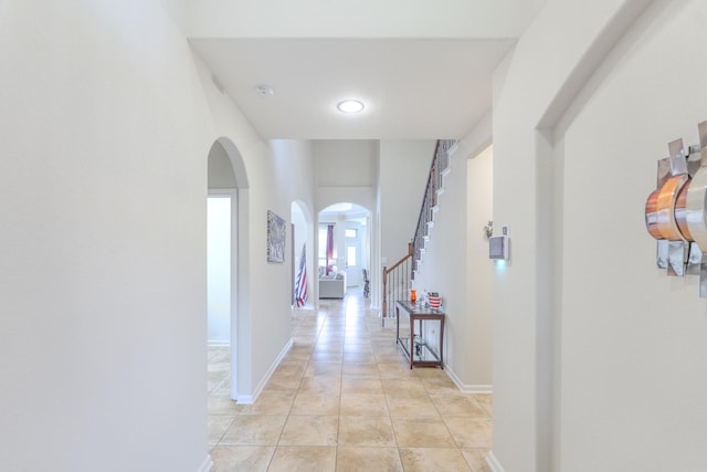 hall with stairway, light tile patterned floors, baseboards, and arched walkways