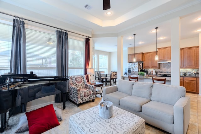 living room with a raised ceiling, light tile patterned floors, a ceiling fan, and visible vents