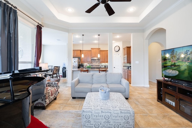 living area featuring light tile patterned floors, ceiling fan, arched walkways, and a tray ceiling