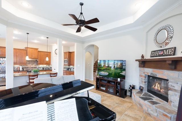 living room featuring a stone fireplace, a raised ceiling, a ceiling fan, and arched walkways