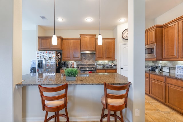 kitchen with under cabinet range hood, a breakfast bar area, stainless steel appliances, and brown cabinets