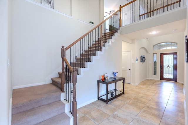 foyer entrance featuring stairs, light tile patterned floors, baseboards, and a towering ceiling