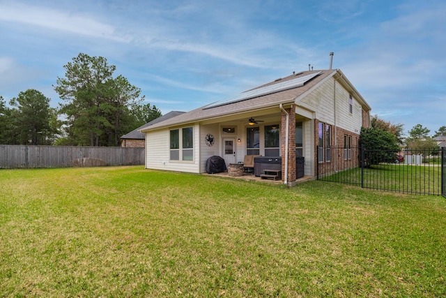 back of property with a ceiling fan, solar panels, a yard, a fenced backyard, and a hot tub