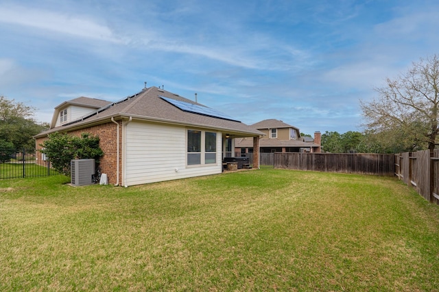 rear view of house with solar panels, a fenced backyard, central air condition unit, a lawn, and brick siding