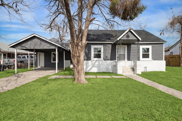 view of front of property with brick siding, fence, roof with shingles, a front yard, and a carport