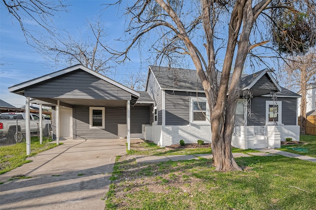 bungalow-style house with a front lawn, driveway, a carport, fence, and brick siding