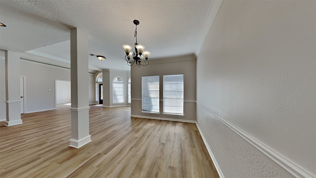 interior space with light wood finished floors, a textured ceiling, decorative columns, and a textured wall