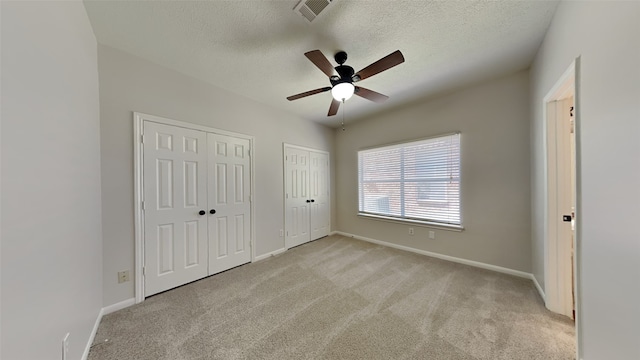 unfurnished bedroom with visible vents, multiple closets, a textured ceiling, carpet flooring, and baseboards