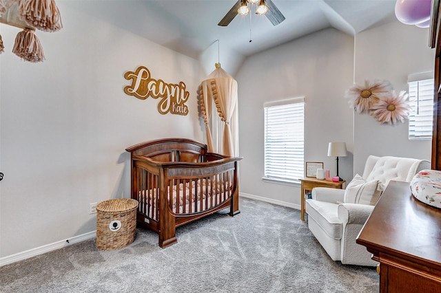 carpeted bedroom with a crib, lofted ceiling, baseboards, and ceiling fan