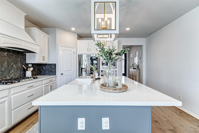 kitchen with premium range hood, light wood finished floors, gas stovetop, stainless steel fridge, and backsplash