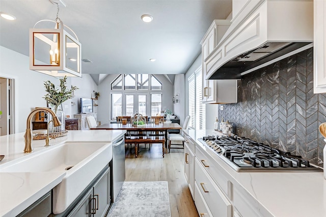 kitchen featuring premium range hood, light wood finished floors, a sink, appliances with stainless steel finishes, and backsplash