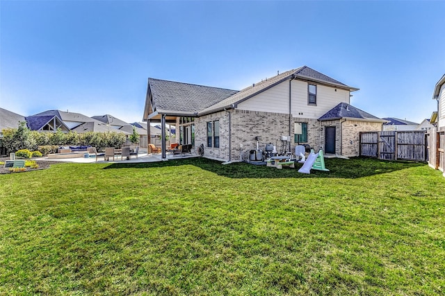 rear view of property with a yard, a patio area, brick siding, and a fenced backyard