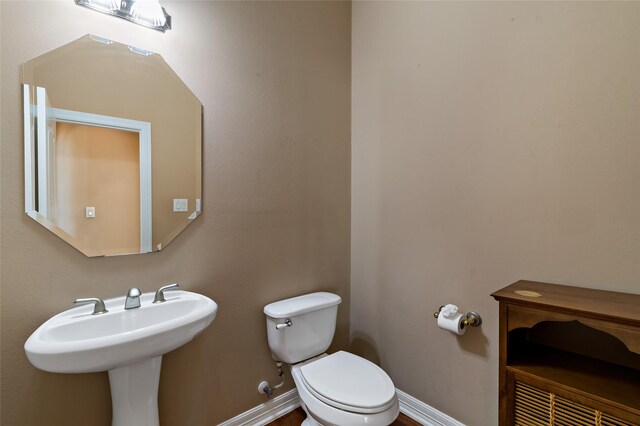 half bath with toilet, baseboards, and a sink