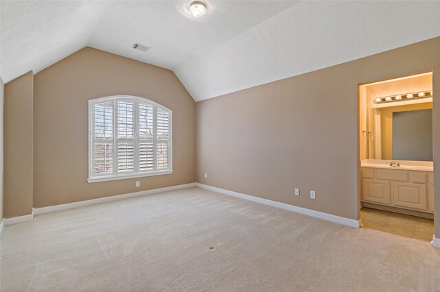 unfurnished bedroom featuring visible vents, light colored carpet, baseboards, and vaulted ceiling