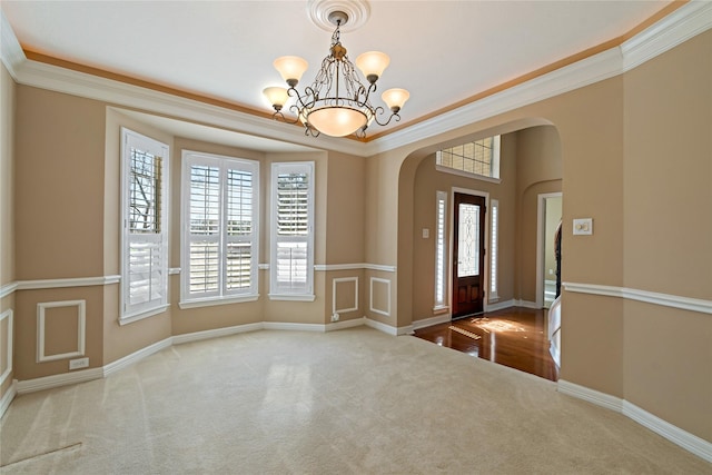 carpeted foyer featuring baseboards, arched walkways, an inviting chandelier, and crown molding