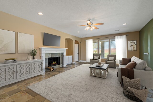 living room featuring a textured ceiling, a high end fireplace, recessed lighting, arched walkways, and ceiling fan