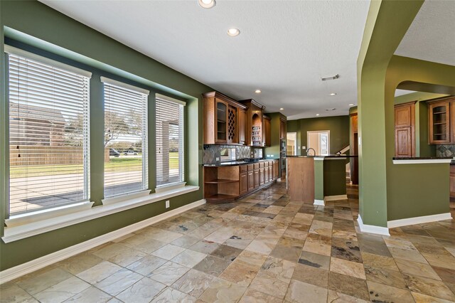 kitchen with glass insert cabinets, tasteful backsplash, visible vents, and baseboards