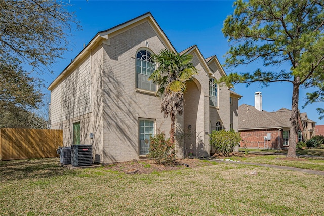 view of side of property with a yard, brick siding, cooling unit, and fence