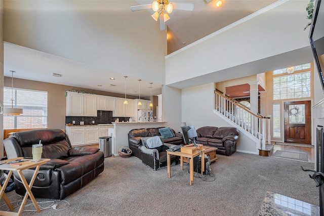 carpeted living area featuring visible vents, stairway, a high ceiling, baseboards, and ornate columns