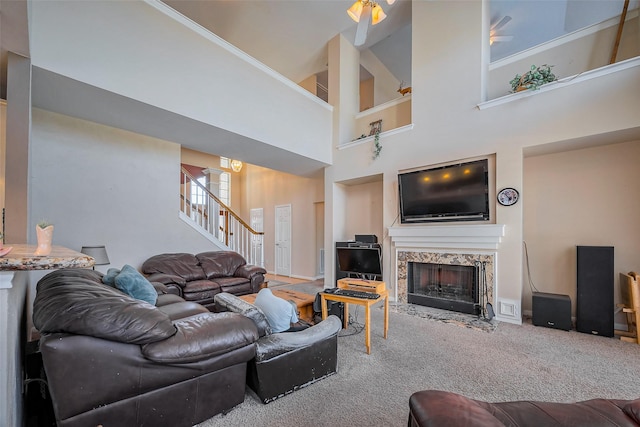 carpeted living room featuring a high end fireplace, stairs, and a towering ceiling