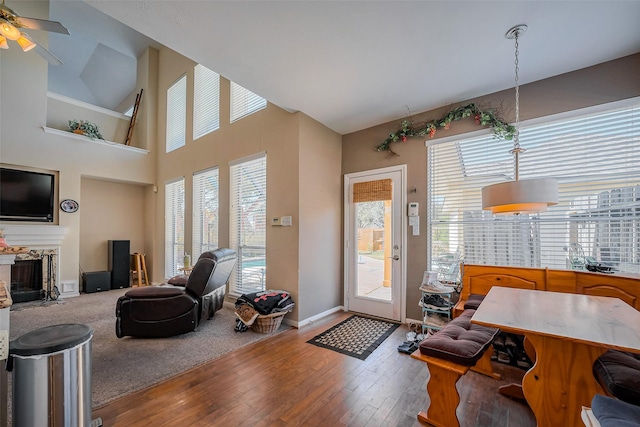 living room featuring ceiling fan, baseboards, a fireplace, a towering ceiling, and hardwood / wood-style flooring