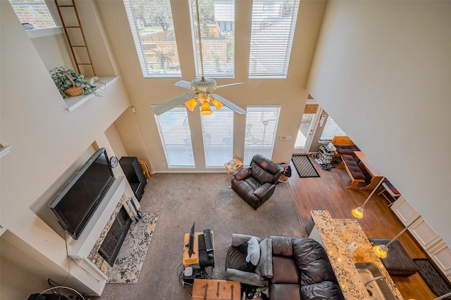 unfurnished living room featuring carpet floors, a high ceiling, a fireplace with raised hearth, and a ceiling fan