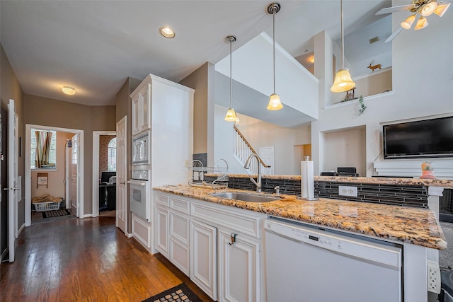 kitchen with dark wood-type flooring, a sink, light stone counters, backsplash, and white appliances