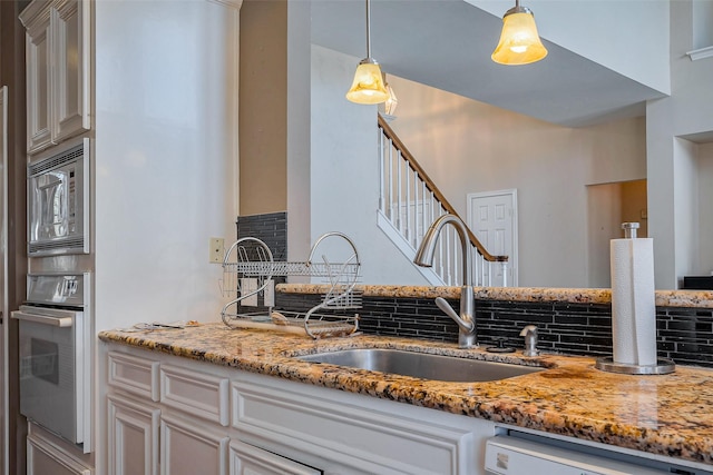 kitchen with light stone countertops, a sink, stainless steel appliances, decorative light fixtures, and tasteful backsplash