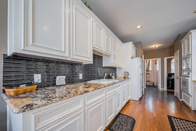 kitchen featuring white appliances, light stone counters, light wood finished floors, white cabinets, and backsplash