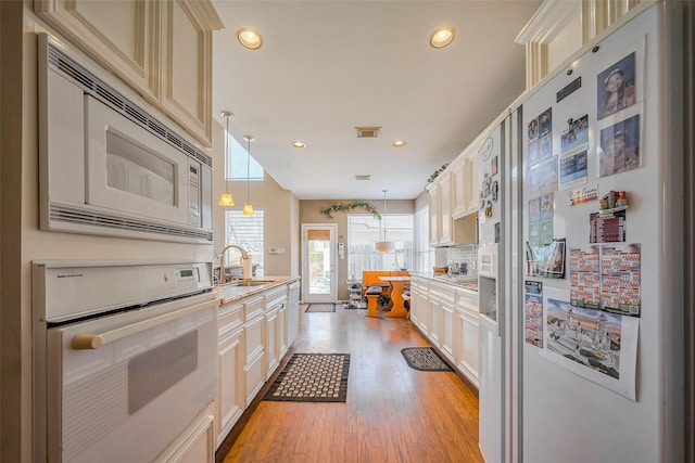 kitchen featuring visible vents, a sink, white appliances, light wood finished floors, and decorative backsplash