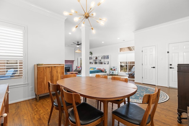 dining space featuring ceiling fan with notable chandelier, crown molding, wood finished floors, and a fireplace