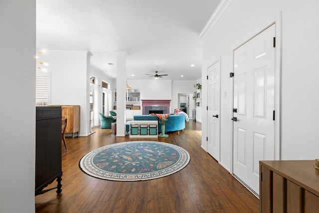 foyer entrance with wood finished floors, decorative columns, a fireplace, ceiling fan, and ornamental molding