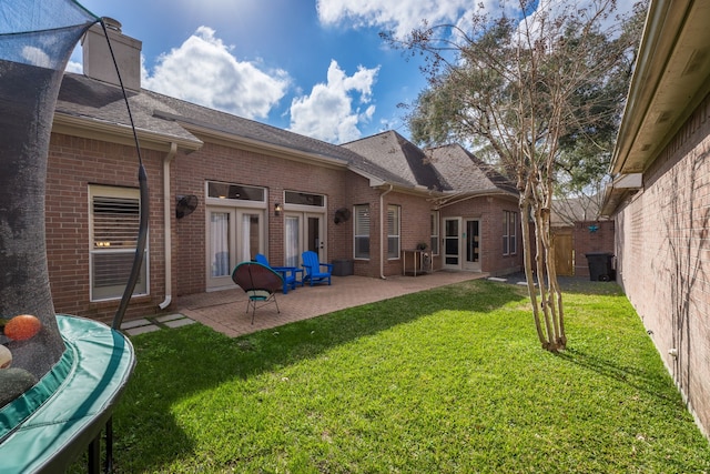 rear view of property featuring a patio, a trampoline, a lawn, and brick siding