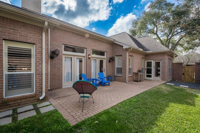 rear view of house featuring brick siding, roof with shingles, a lawn, a patio area, and a gate