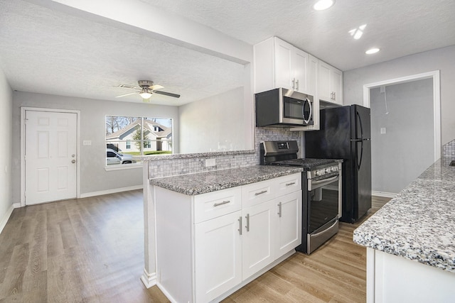 kitchen featuring light stone counters, stainless steel appliances, decorative backsplash, white cabinets, and light wood-type flooring