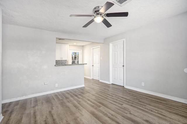 spare room featuring a ceiling fan, visible vents, wood finished floors, baseboards, and a textured ceiling