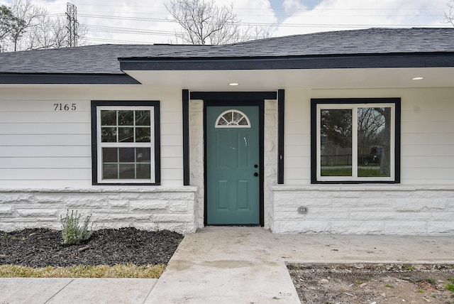 property entrance featuring stone siding and roof with shingles