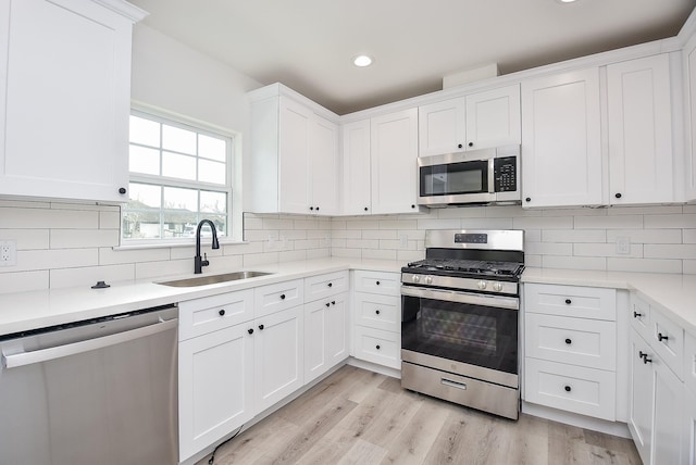 kitchen featuring light wood-style flooring, tasteful backsplash, appliances with stainless steel finishes, and a sink