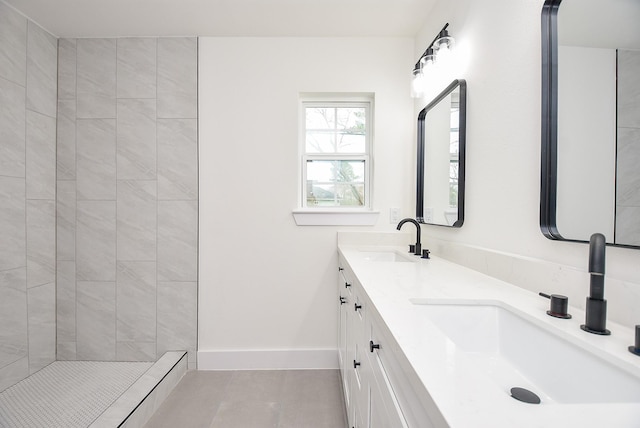 bathroom with a tile shower, double vanity, baseboards, and a sink