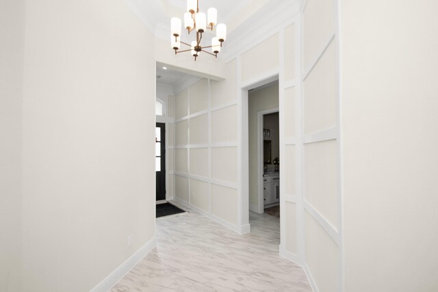 hallway with an inviting chandelier, a decorative wall, baseboards, and marble finish floor