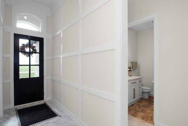 foyer featuring a decorative wall, marble finish floor, and ornamental molding