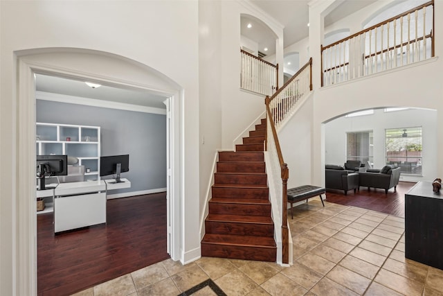 stairway with wood finished floors, arched walkways, a high ceiling, crown molding, and baseboards